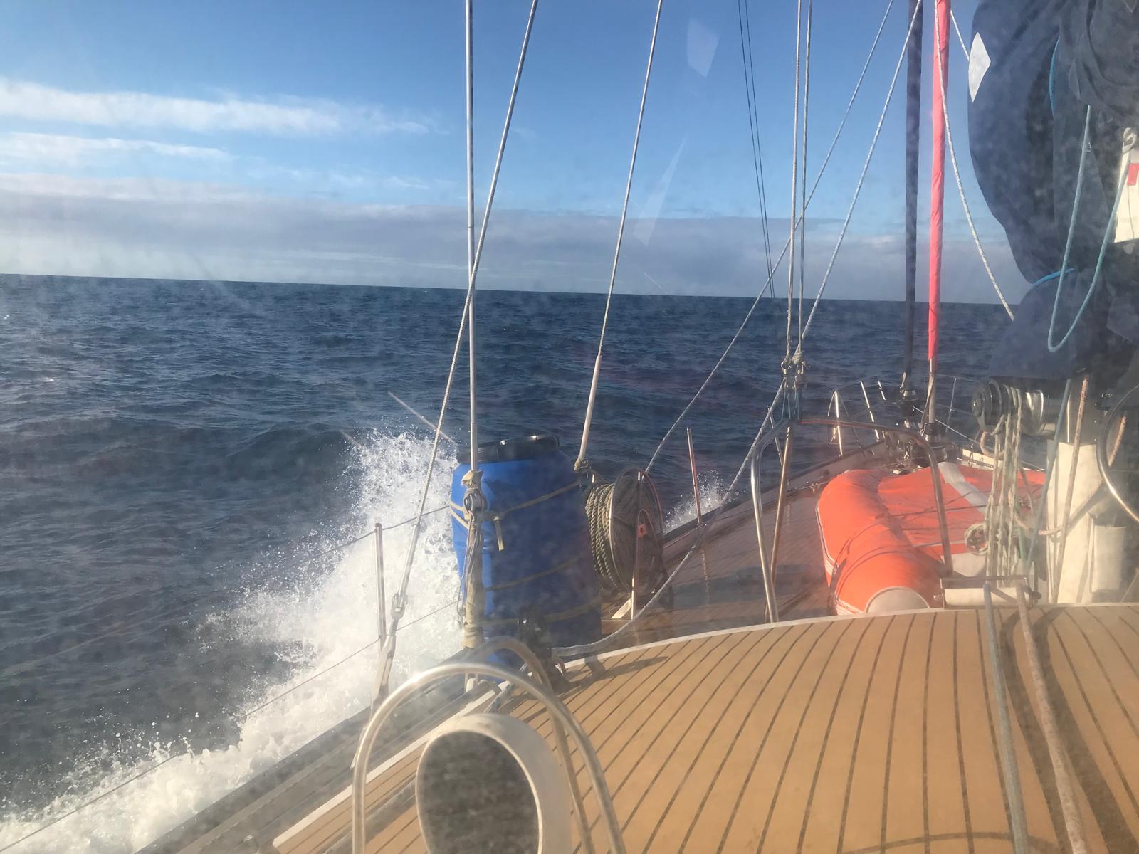 Reaching in a fresh breeze. Spray over the weather rail, the boat sailing herself, teak deck dry to leeward.