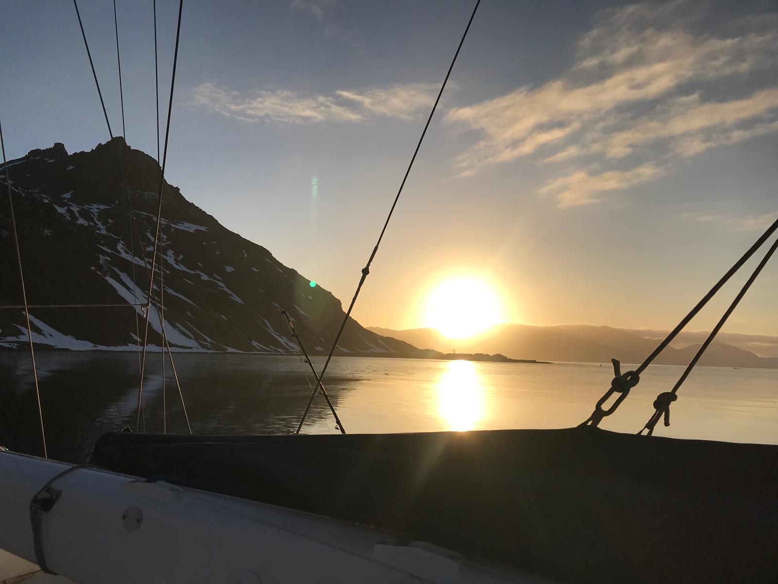 Sunset from the anchorage, framed by the rigging. Flat calm, the sun setting into a gap in the hills.