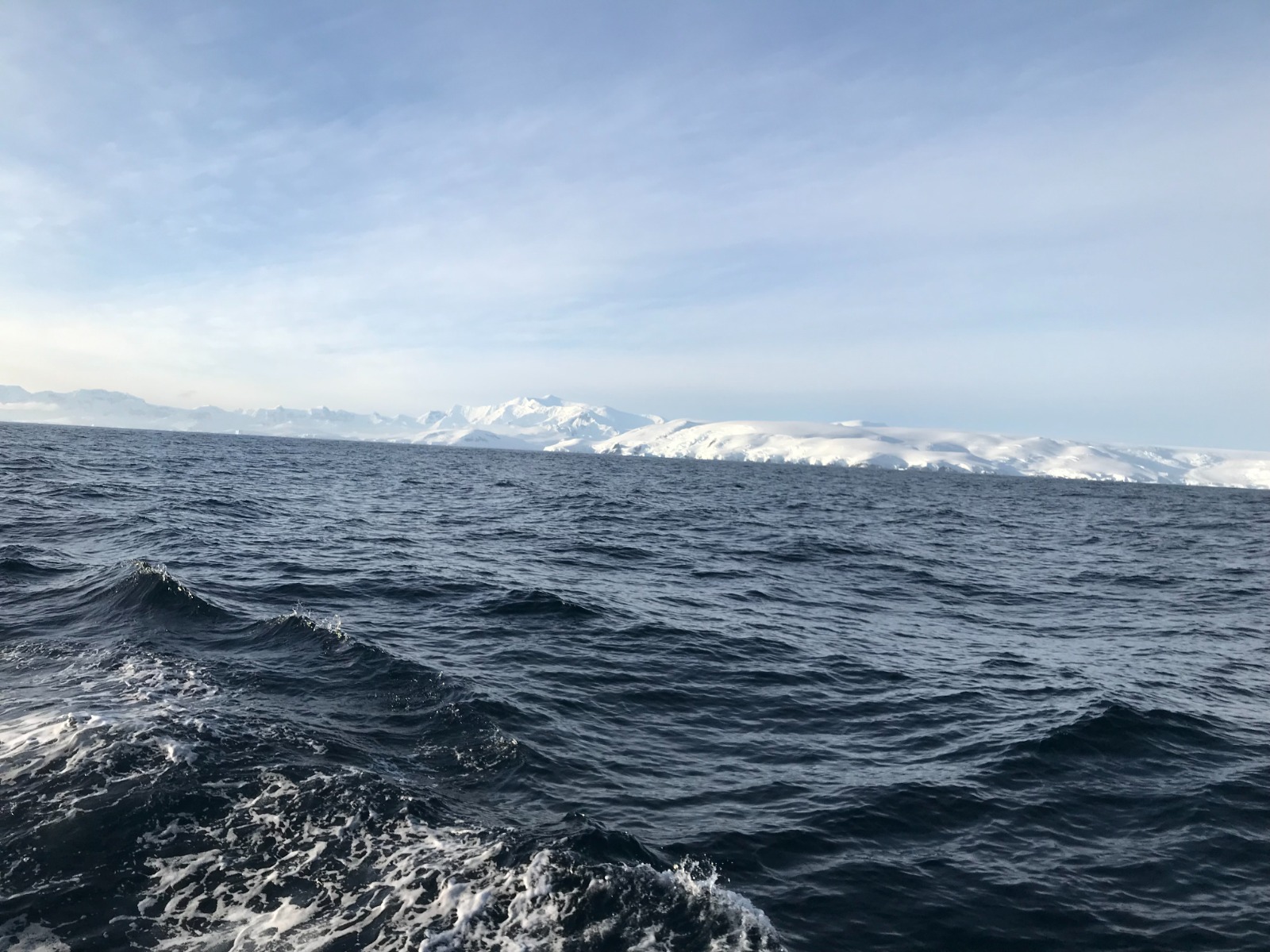 The ice coast from offshore. An ice cap running down to a cliffed edge, mountains behind, a short sea running.