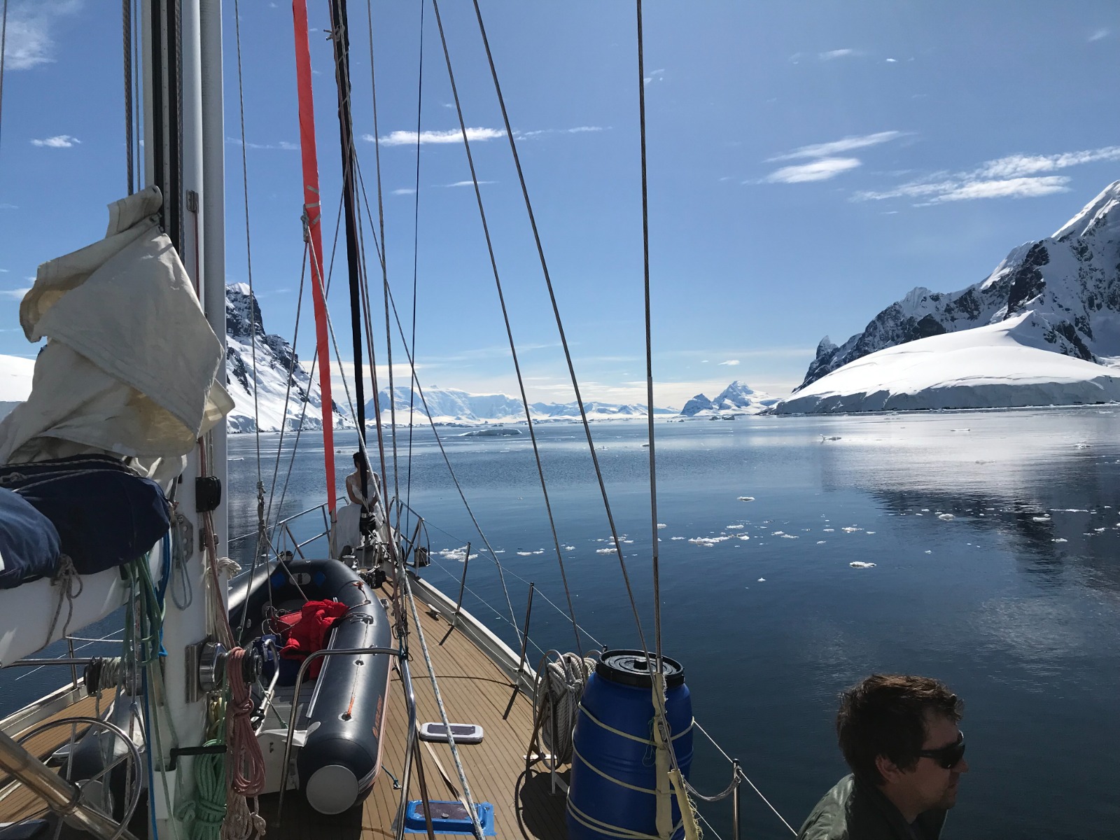 At anchor. Sails harbour-furled, RIB on the sidedeck, ice drifting past, one of the crew in the cockpit.